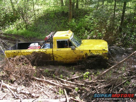 1986 Jeep J-10 pickup truck stuck in mud on a wooded trail