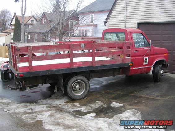 red flatbed truck with wooden sides, writing on window says 14 32 2165 1800
