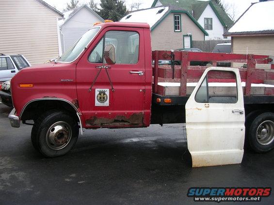 Red flatbed truck with a detached white door lying on the ground, showing significant rust on the lower body