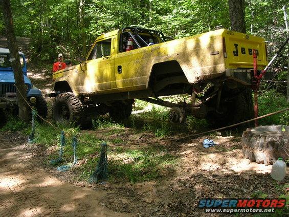 Yellow 1986 Jeep J-10 pickup truck with roll cage on off-road trail
