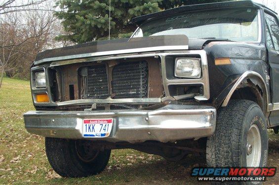 Black Ford F-150 truck front end with missing grille and damaged fender