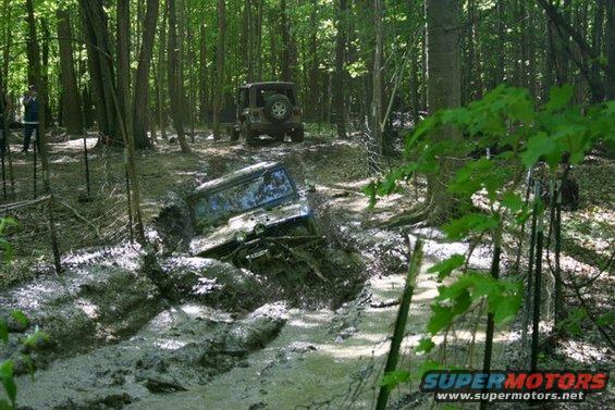 Off-road vehicle stuck deep in mud on a wooded trail