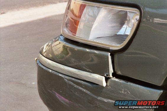 Damaged front corner of a dark green 2000 Mercury Grand Marquis with a broken bumper trim