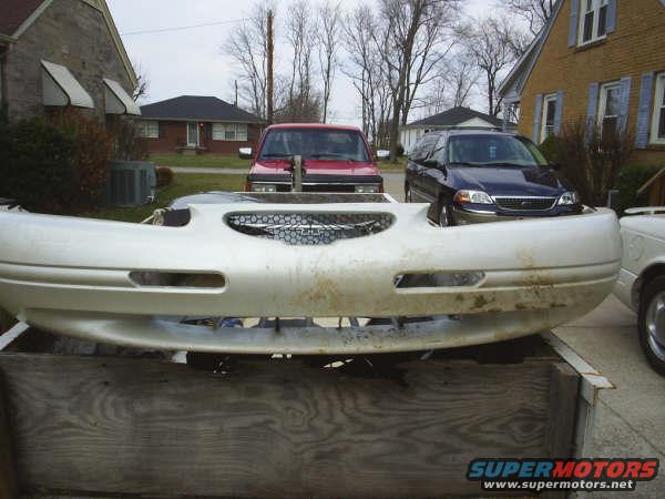 Front bumper on a wooden surface, with a red truck and a dark minivan behind it