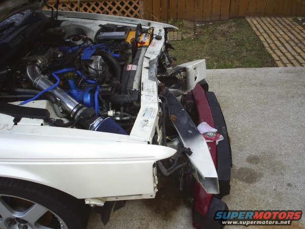 1996 Ford Thunderbird engine bay with aftermarket intake, front end damaged, parts piled up