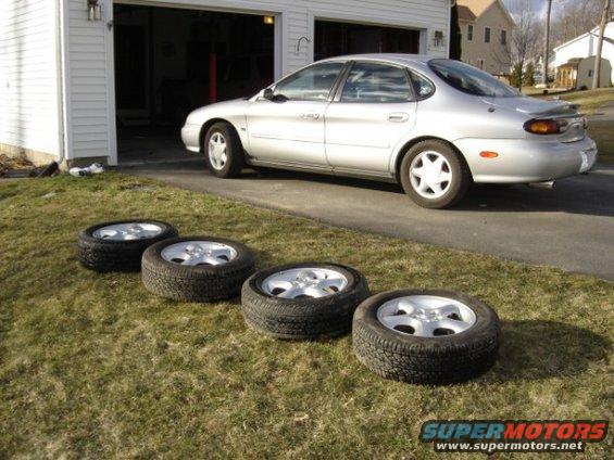 Silver sedan parked in driveway with four tires lined up on the grass in front
