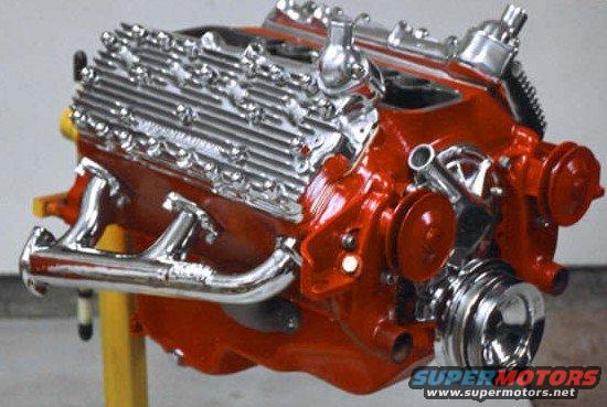 Red V8 engine with chrome valve covers and exhaust manifolds, mounted on a yellow stand