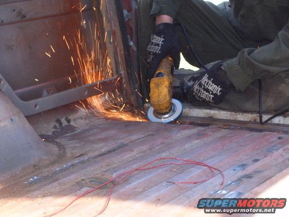 Person wearing Mechanix gloves uses an angle grinder on the rusty floor of a vehicle interior