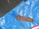 1979 Ford Bronco - A single rusty metal linkage part with two holes is shown on a blue tarp, likely a component for a vehicle.