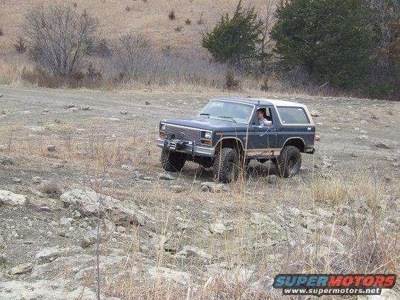 Dark blue Ford Bronco with a white top drives on a rocky, dry terrain