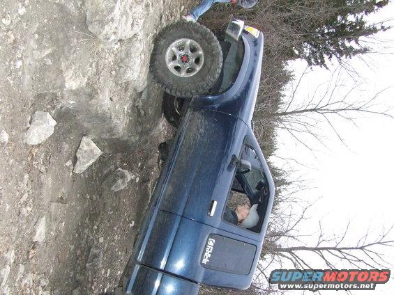 Blue pickup truck with one wheel up on rocks, driver inside