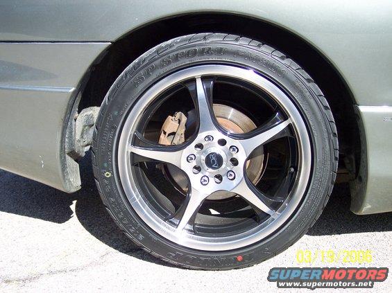 Close-up of a car's rear wheel with a custom five-spoke rim and Dunlop SP Sport tire. Brake rotor and caliper visible behind the wheel