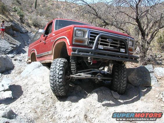 Red Ford Bronco with lifted suspension and bull bar navigating rocky terrain