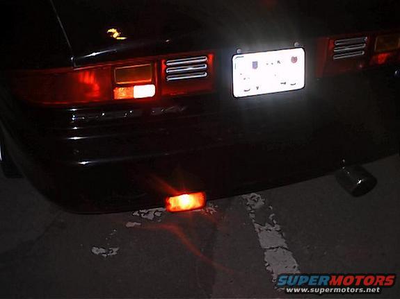Rear view of a dark-colored car showing taillight, license plate, and exhaust tip