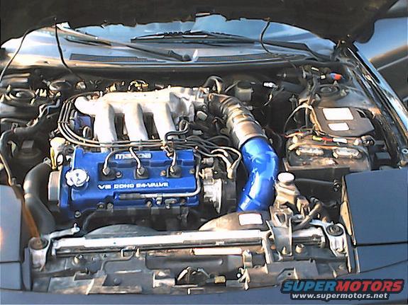 Engine bay with blue V6 DOHC 24-valve Mazda engine, blue intake pipe, and battery