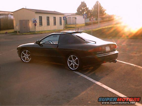 Black 1994 Ford Probe parked on asphalt with a building and sun in background