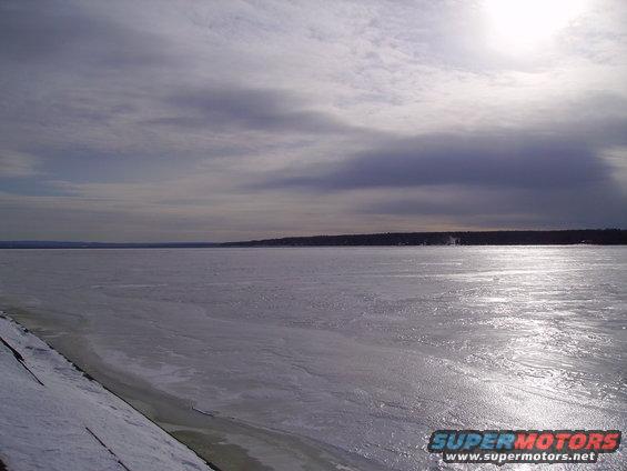 Frozen lake or river under a cloudy sky with sun glare