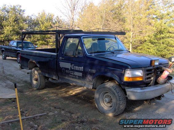 Dark blue 1995 Ford F-250 pickup with a rack in the bed, parked next to another truck