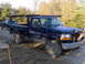 1995 Ford F-250 - A dark blue Ford F-250 pickup truck, equipped with a rack, is parked on a dirt lot next to another truck.