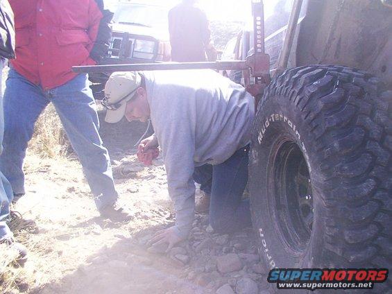 Guy jacking up a large tire on an off-road vehicle, another vehicle visible behind