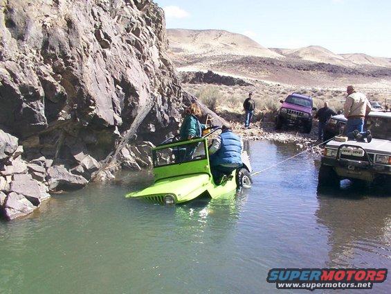 Green Jeep partially submerged in water, being towed by a silver SUV