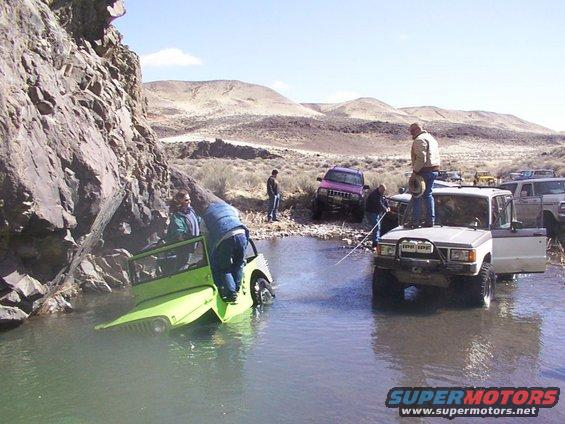 Off-road vehicles navigating a stream with people around
