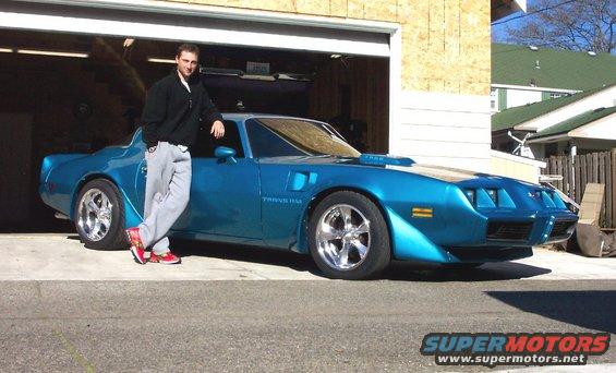 Man leaning on a blue 1979 Pontiac Trans Am parked in front of an open garage