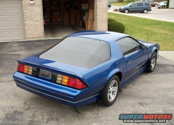 Blue third-gen Camaro parked in driveway, rear quarter view. Garage in background