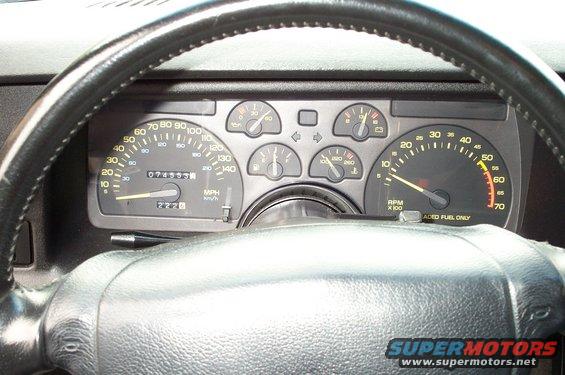 Car dashboard with speedometer, tachometer, and other gauges. Odometer reads 074555. Steering wheel is black