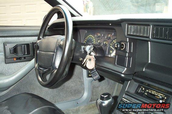 Interior shot of a 1990 Chevrolet Camaro, showing the steering wheel, dashboard gauges, and center console