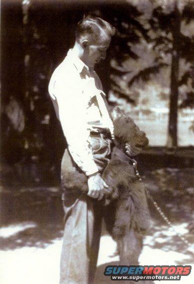 Man holding a shaggy dog outdoors, with trees in the background
