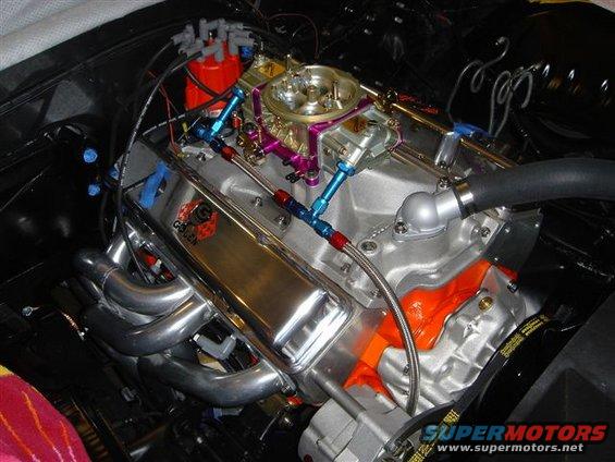 Close-up of a V8 engine with chrome valve covers, aftermarket carburetor, and headers