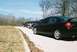 2004 Dodge SRT-4 - A line of cars, including a black Dodge Neon SRT-4, are parked on a paved road with trees in the background.
