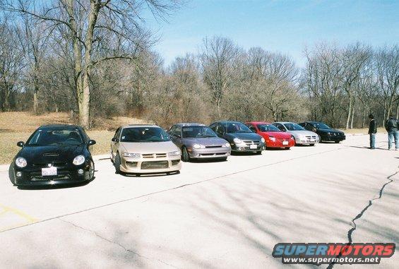 several cars parked in a line on a sunny day, trees in background