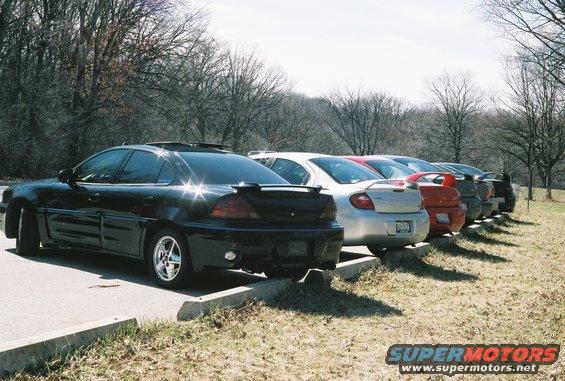 Several sedans parked in a row, including a black Grand Am and a silver Neon