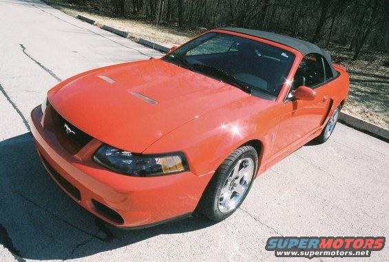 Red convertible sports car with black top, hood scoops, and chrome wheels parked on asphalt