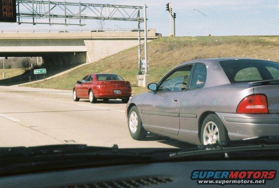 Gray coupe side view on highway, red sedan in background