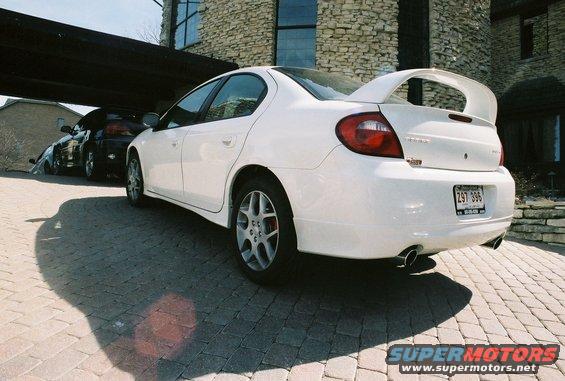 White 2004 Dodge Neon SRT-4 with a large rear spoiler parked on a brick driveway, another car visible behind it