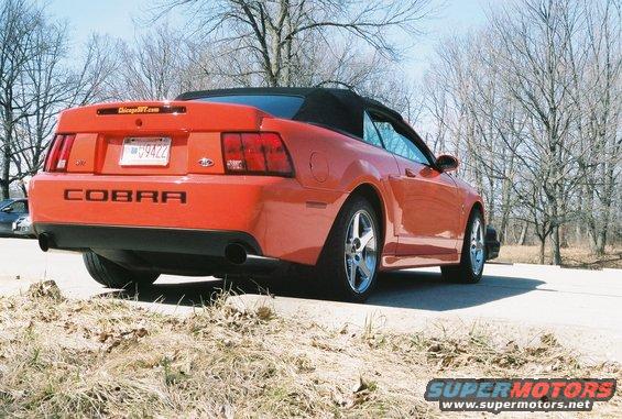Orange convertible Mustang Cobra parked outdoors, rear view. License plate reads 09422