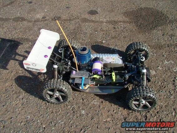 Remote control car with a blue engine and white spoiler, sitting on gravel