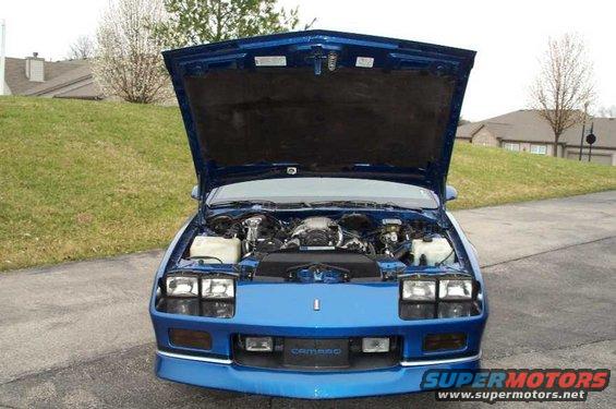 Blue Chevrolet Camaro with hood open, showing the engine bay. The word "CAMARO" is visible on the front