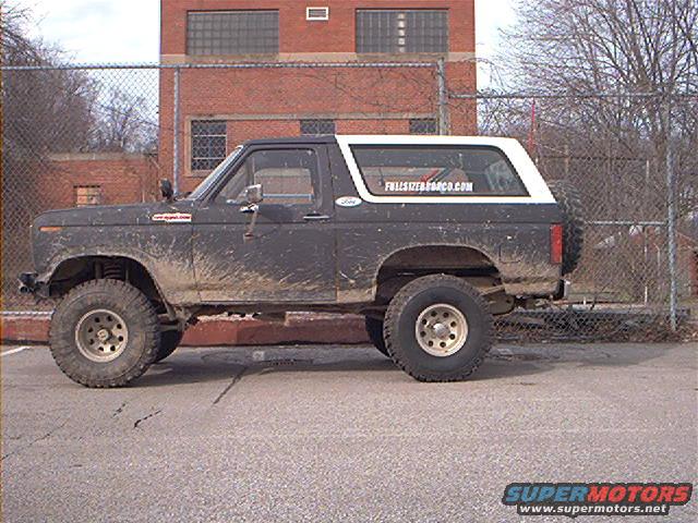Mud-splattered dark gray 1978 Ford Bronco with a white top, lifted suspension, and off-road tires, seen from the side