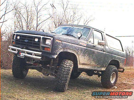 Mud-splattered Ford Bronco lifted with large tires, parked on uneven ground