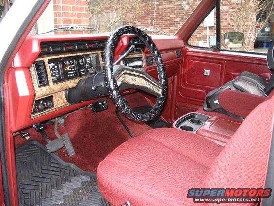 Interior of a truck with red seats, dashboard, and door panels. Features a black steering wheel with a patterned cover and a center console with cup holders