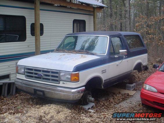 1988 Ford Bronco, blue and white, missing wheels, parked next to RV