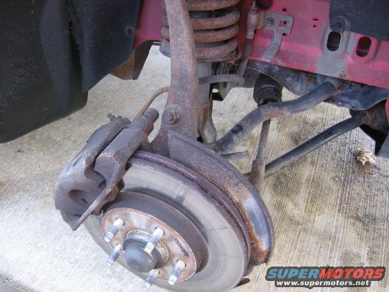 Front suspension and brake assembly with rust. Supermotors.net logo visible