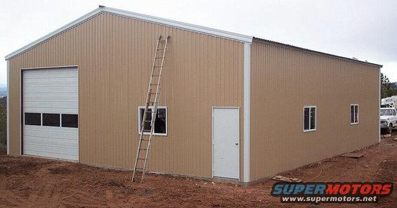 Tan metal building with a large garage door, a ladder leaning against it, and a white truck parked to the right