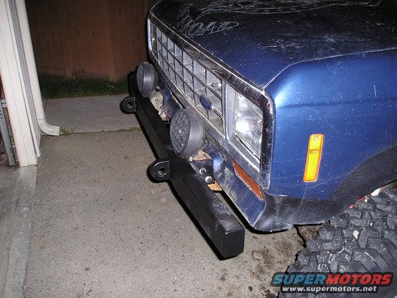 Blue SUV front bumper with two auxiliary lights and tow hooks. Grille visible