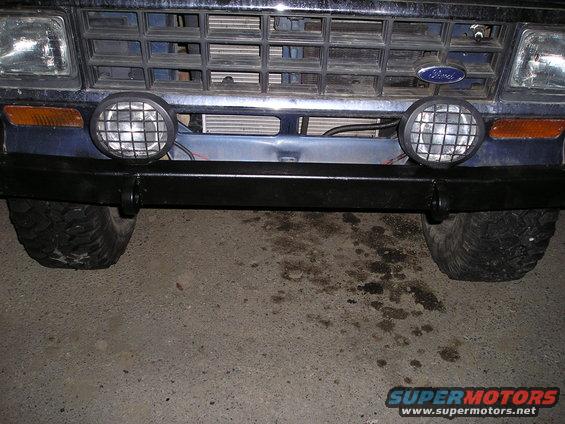 Front of a blue Ford truck with a black bumper and two round fog lights. Ford logo visible on grille