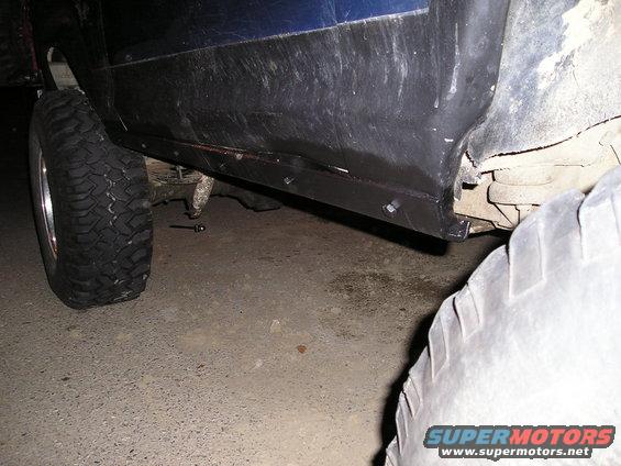 Blue vehicle side panel with black trim and large tire. Undercarriage visible